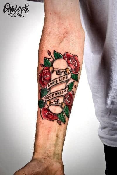 Tatuagem de um skate no antebraço rodeado por rosas e folhas com a frase "Long Lice Your Dreams"