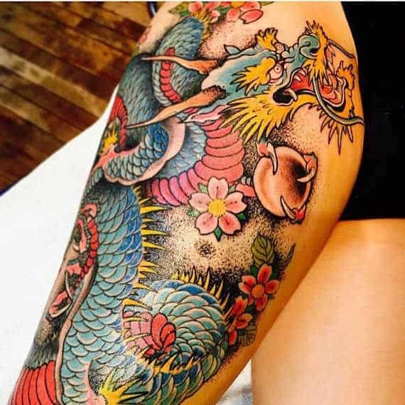 Tatuagem de um dragão oriental azul voando feito na perna de uma mulher 
