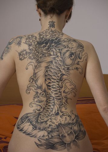 Tatuagem grande nas costas de uma mulher feita em preto e branco de uma carpa saindo da água 