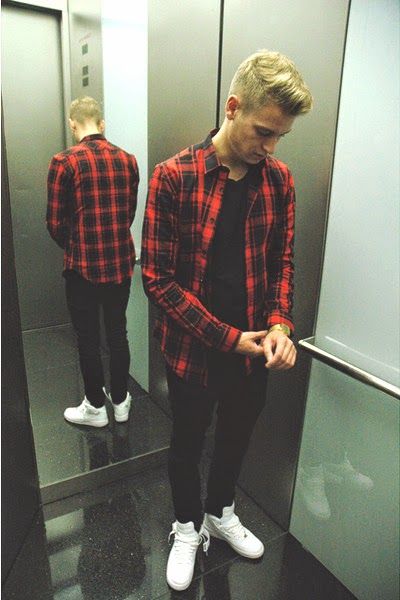 Homem dentro de um elevador abotoando sua camisa xadrez vermelha no pulso 