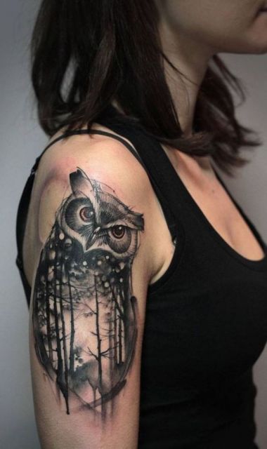 Tatuagem no braço de uma mulher de uma coruja vista de frente com uma floresta no interior de seu corpo