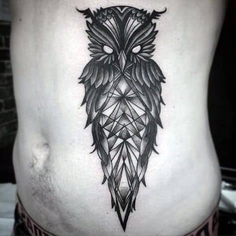 Tatuagem na costela de um homem com o desenho de uma coruja muito sombria feita a partir de formas geométricas. 
