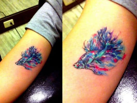 Tatuagem feita com aquarela de um peixe beta com diversas tonalidades de cor enquanto nada com longas barbatanas 