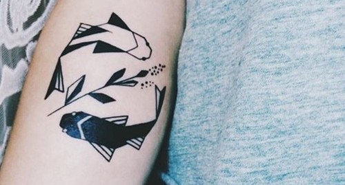 Tatuagem geométrica de dois peixes em cores e posições opostas separados por uma flor 