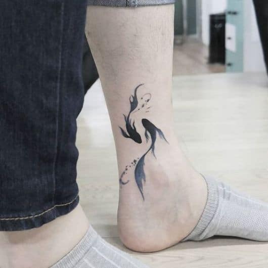 Tatuagem no tornozelo com o desenho delicado de dois peixes betas nadando em posições opostas 