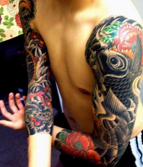 Tatuagem de carpa no estilo oriental feita nos dois braços de um homem cobrindo-os completamente em tons de preto 