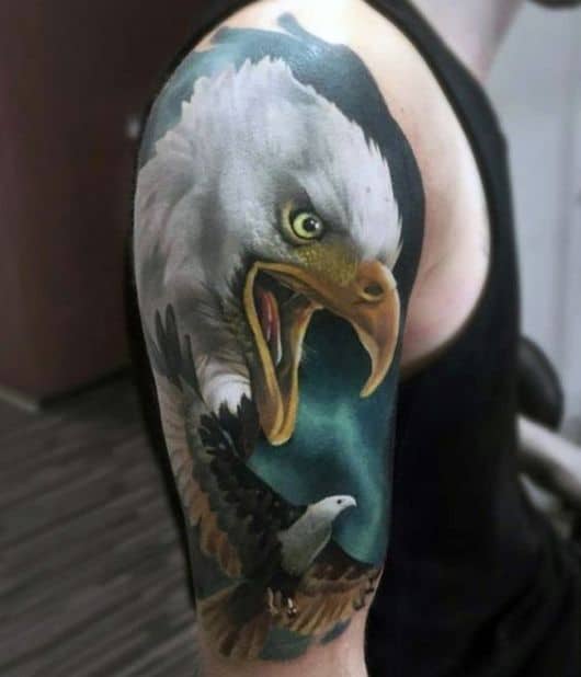 Tatuagem que vai do topo do ombro até metade do braço com o rosto de uma águia real de bico aberto e uma outra águia menor voando