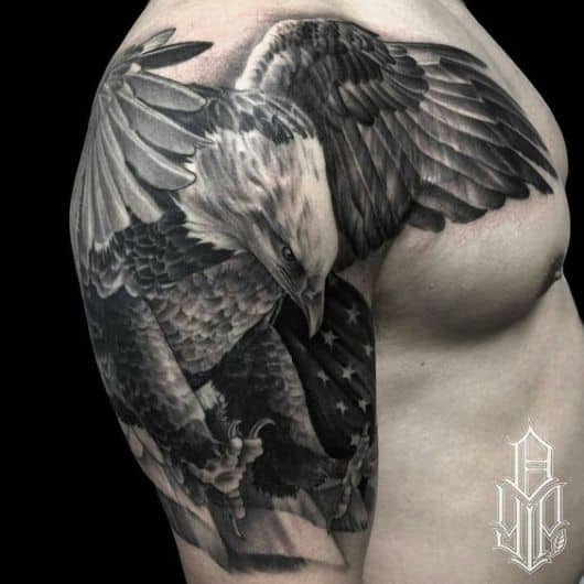 Tatuagem que cobre o ombro e parte do peito de um homem com o desenho de uma águia realista pronta para abater sua presa 
