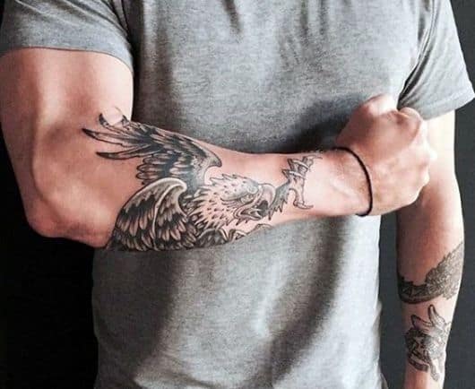 Tatuagem no antebraço com o desenho de uma águia real no estilo tradicional pronta para atacar