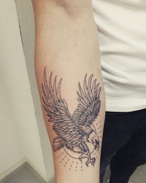 Tatuagem pequena no antebraço de uma águia voando e o sol atrás dela
