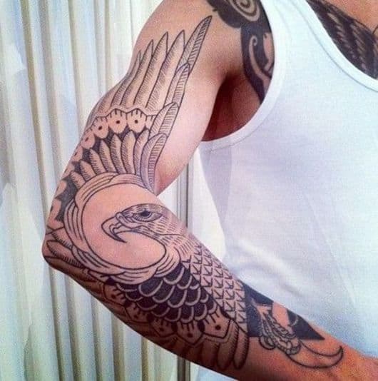 Tatuagem de águia no braço que utiliza a asa do animal para cobrir o espaço que ficaria em branco 