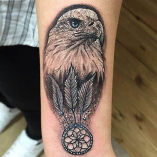 Tatuagem da cabeça de uma águia olhando para o horizonte com um apanhador de sonho onde seria seu peito