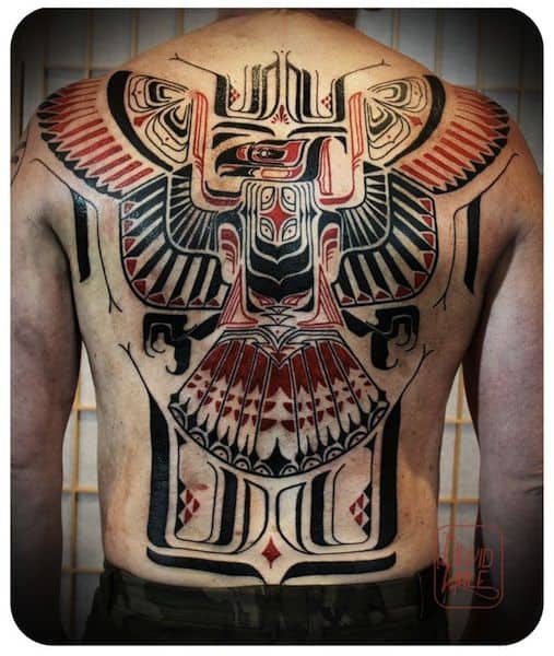 Tatuagem cobrindo as costas inteiras de um homem com o desenho tribal de uma águia vista de frente com as duas asas abertas lembrando muito inscrições indígenas antigas 