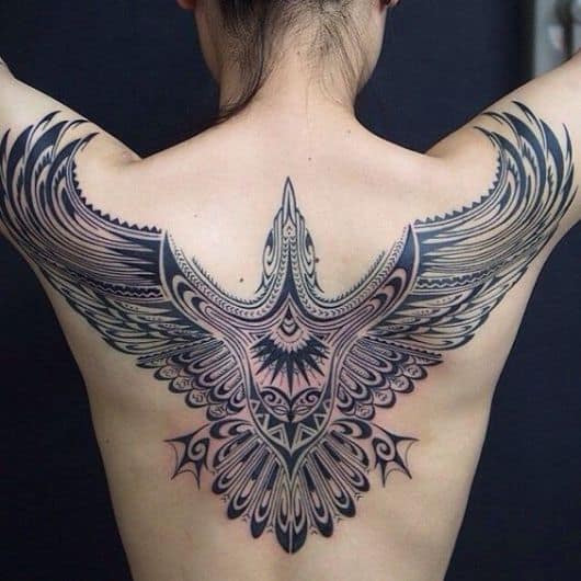 Tatuagem grande nas costas de uma mulher com o desenho tribal de uma águia com as asas abertas 
