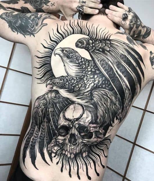 Tatuagem grande nas costas de duas águias repousando em cima de uma crânio 