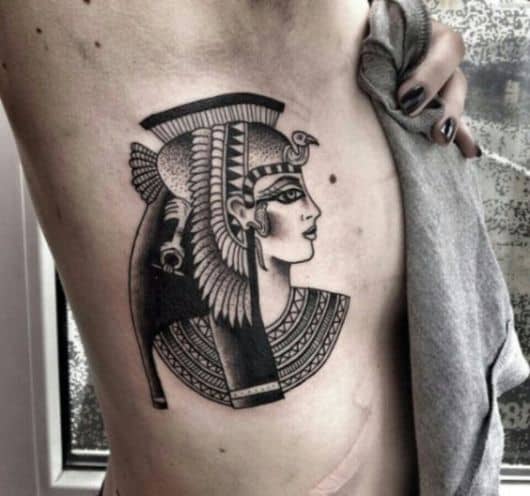 Tatuagem em tons de cinza da deusa Isís olhando para o lado com diversos enfeites em seu cabelo. 