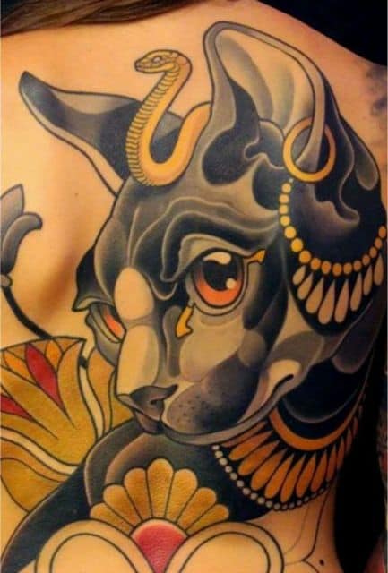 Tatuagem grande de um gato preto com diversos adornos feita nas costas de uma mulher 
