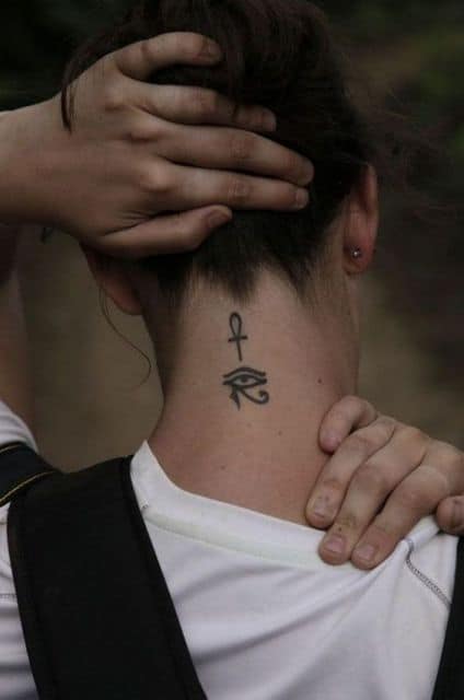 Tatuagem delicada do Olho de Hórus e da cruz Ankh feita na nuca de uma mulher. 