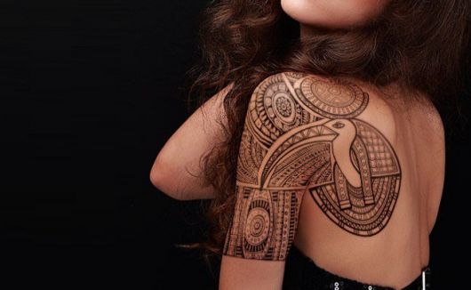 Tatuagem nas costas e parte do braço de uma mulher com diversas formas que constituem adornos egípcios. 