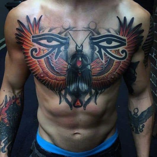 Tatuagem no peito de um homem com um escaravelho grande e dois olhos de hórus, um de cada lado. 