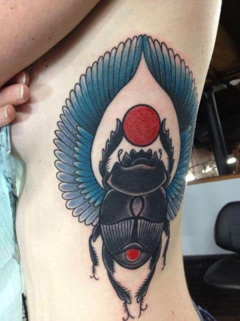 Tatuagem na costela com o desenho de um escaravelho com asas e o sol entre suas patas. 