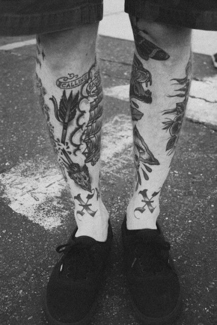 Foto das duas canelas de um homem com diversas tatuagens, todas em tons de preto.