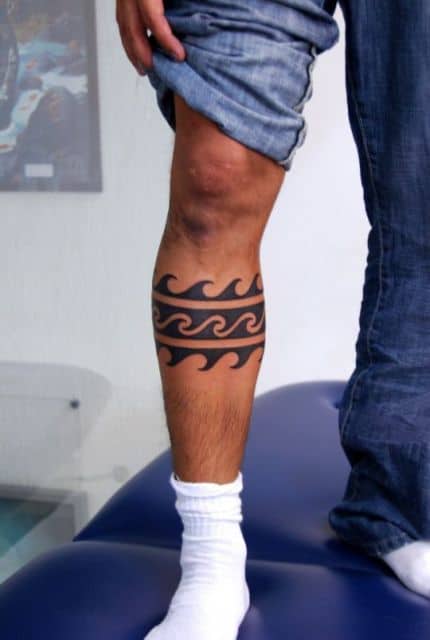 Tatuagem na canela de formas pintadas de preto que formam as ondas do mar. 