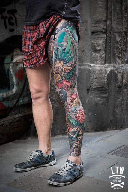 Tatuagem oriental cobrindo toda a perna de um home. Ela é composta por diversos elementos coloridos da cultura oriental. 