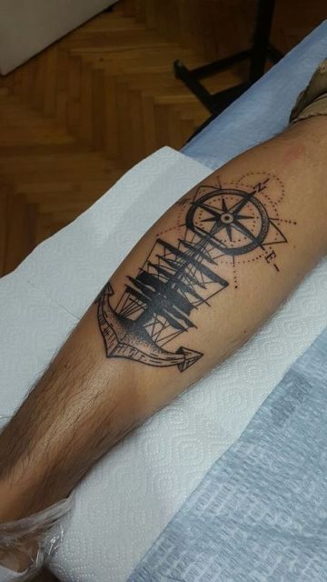 Tatuagem na panturrilha de um navio com uma bússola acima dele e uma âncora abaixo.