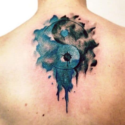 Tatuagem nas costas com um Yin Yang em aquarela, onde as cores azul e preto se contrapõem. 