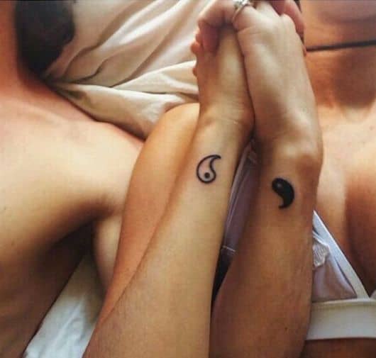 Foto de um casal de mãos dadas. No pulso de cada há uma metade do Yin Yang. 