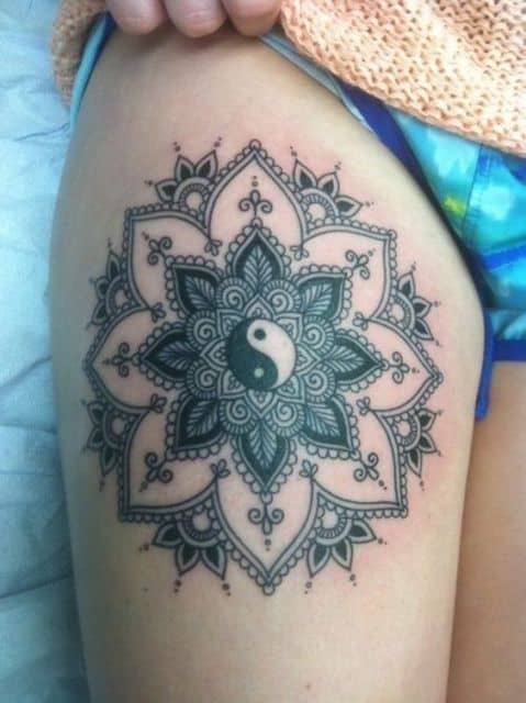Tatuagem grande na coxa de uma mandala similar a uma flor com um Yin Yang no centro. 