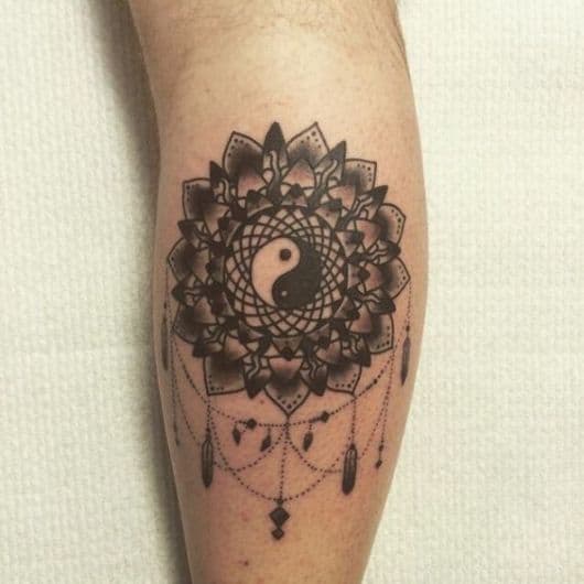 Tatuagem na canela de uma mandala com adornos e um Yin Yang no centro. 