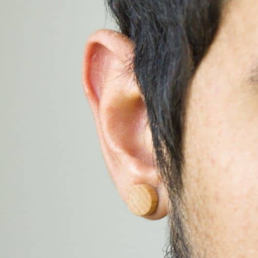 Foto tirada próxima da orelha de um homem usando um alargador de pressão de madeira. 