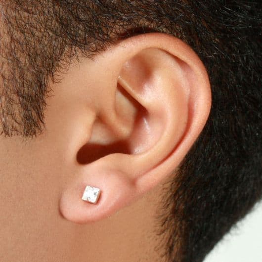 Foto em close up da orelha de um homem usando um brinco de pressão masculino discreto.