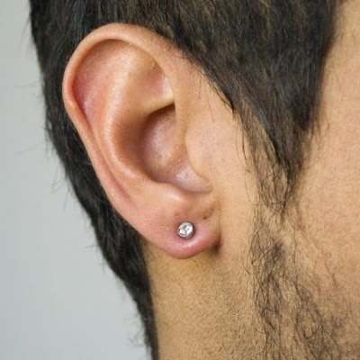 Foto em close up da orelha de um homem usando um brinco de pressão discreto.