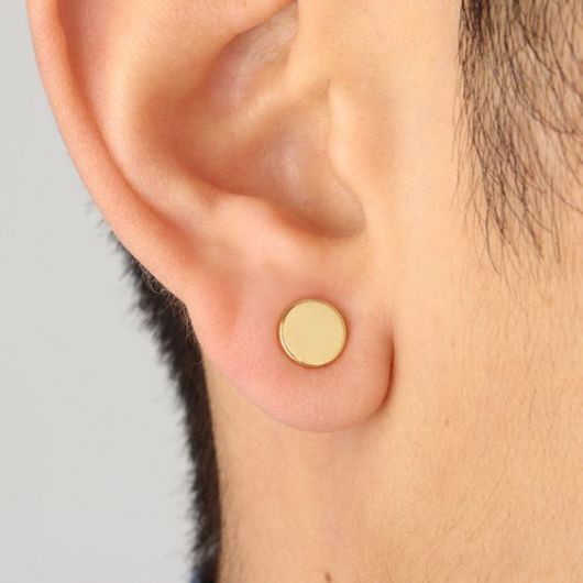 Foto em close up de um brinco de pressão dourado na orelha de um homem.