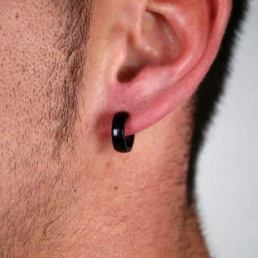 Foto em close up da orelha de um homem usando um brinco de argola de pressão preto.