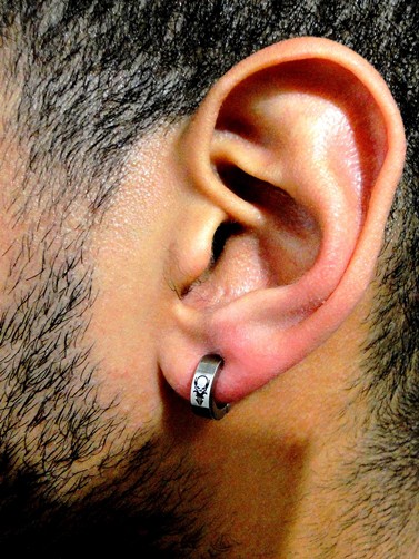 Foto em close up da orelha de um homem com um brinco de argola de pressão com um pequeno desenho detalhado. 