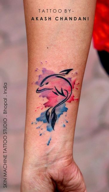 Tatuagem de um golfinho saltando com o fundo explodindo em diversas cores de aquarela. 