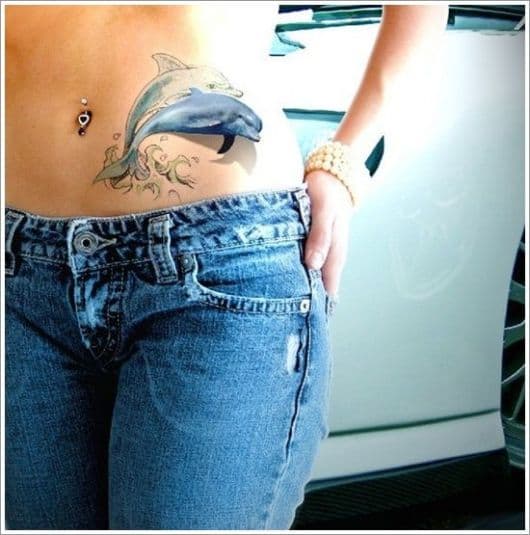 Tatuagem de golfinho feita na cintura de uma mulher com ele saltando da água pintado de azul 