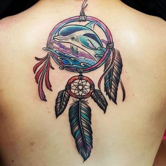 Tatuagem colorida de um golfinho saltando de dentro de um apanhador de sonhos. 