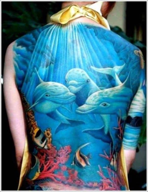 Tatuagem fechando completamente as costas com o desenho do fundo do mar onde há três golfinhos unidos no centro. 