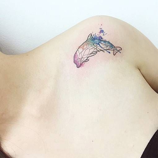 Tatuagem geométrica de um golfinho no ombro com diversas cores de aquarela colorindo-a. 