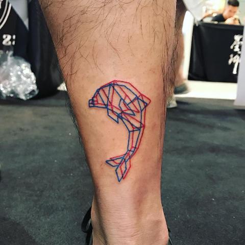 Tatuagem da silhueta de um golfinho na perna que se divide em duas, uma em linhas azuis outra em linhas vermelhas. 
