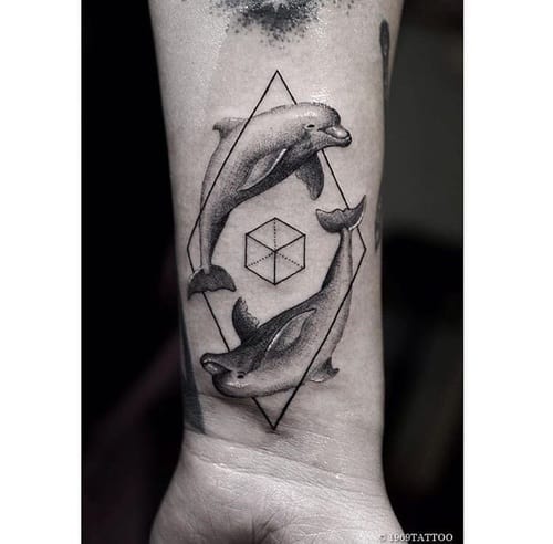 Tatuagem de dois golfinhos em posições opostas limitados por um losango com um símbolo geométrico ao centro.  