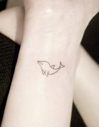 Tatuagem de golfinho delicada no pulso com somente sua silhueta.