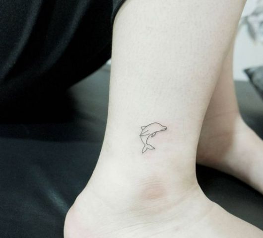 Tatuagem delicada da silhueta de um golfinho saltando feita no calcanhar