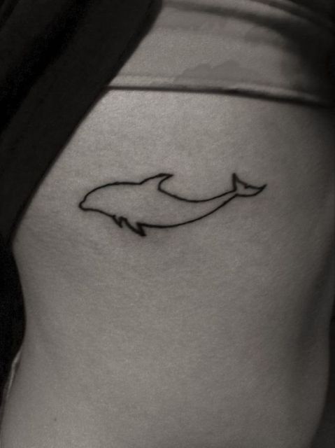 Tatuagem delicada da silhueta de um golfinho feita no costela