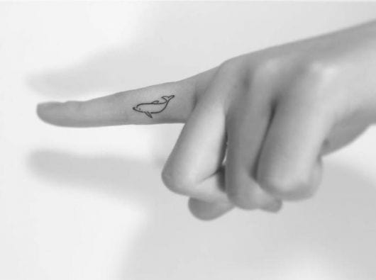 Tatuagem delicada de golfinho muito pequena feita na lateral do dedo indicador.